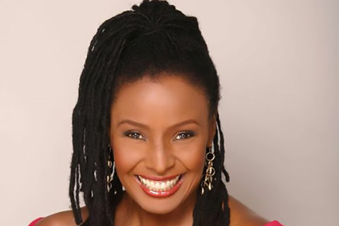 B. Smith. Black woman with long dark locs pulled into high ponytail, wearing off-the-shoulder top. 