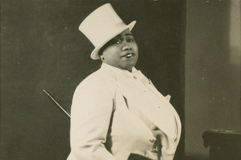 Gladys Bentley. Black woman wearing white top hat and white tuxedo with cane.