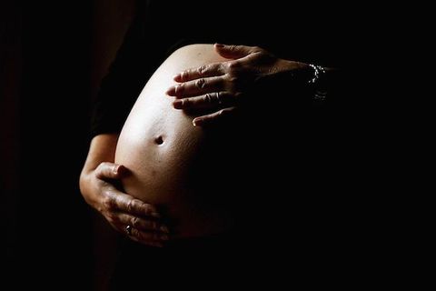 Two hands hold a pregnant stomach against a black background