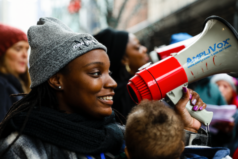 Dashara, a Black woman with a baby strapped to chest, holds a red megaphone at the Walmart protest.
