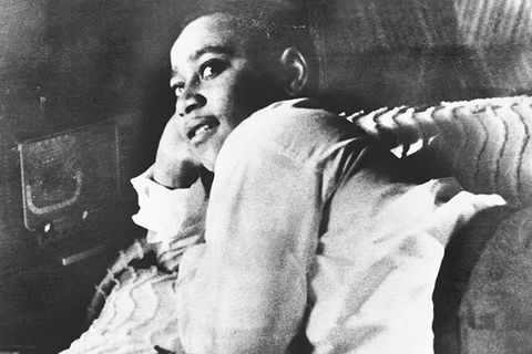 Emmett Till. Archival photo of young Black boy reclining on a bed with his head in right hand, wearing a white shirt and dark pants.
