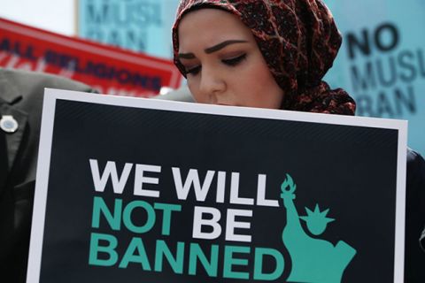 Muslim Ban. Muslim woman wearing brown headscarf and carrying a sign reading "We will not be banned"