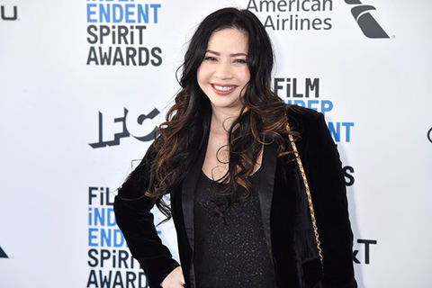 Nina Yang Bongiovi. Asian woman with long dark hair wearing a black jacket and black top standing in front of step and repeat.