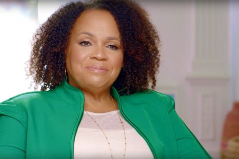 Lisa Price. Black woman with brown shoulder length curly hair wearing white top and green jacket.