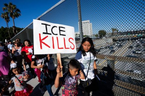 A young boy stands at a protest and holds a sign that reads "ICE KILLS" 