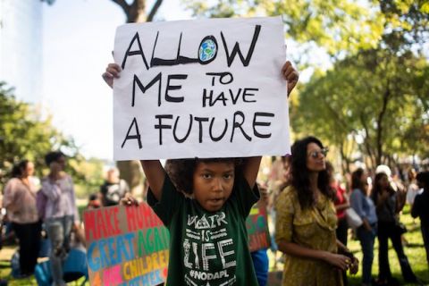Black child in black shirt at protest holds white sign that reads, "Allow me to have a future."