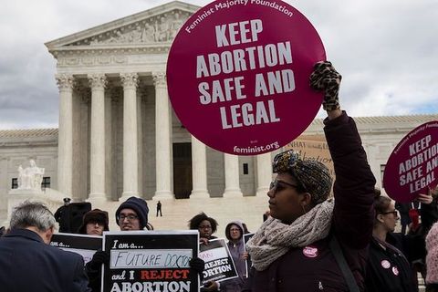 A group of protestors, one holding a sign that reads "Keep Abortion Safe and Legal" stand in front of the Supreme Court of the United States.