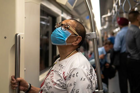 COVID-19. Asian American wearing blue medical mask and white T-shirt stands on train holding pole.