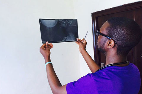 Medical Professional. Black person wearing blue hospital scrubs turned away looking at screen.