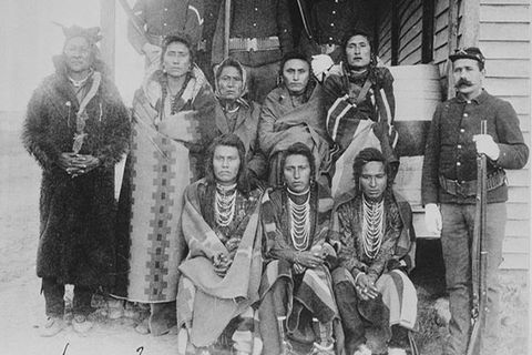 Native Americans. Archival black and white image showing seven Native Americans on a porch, next to a White man wearing an army uniform. 