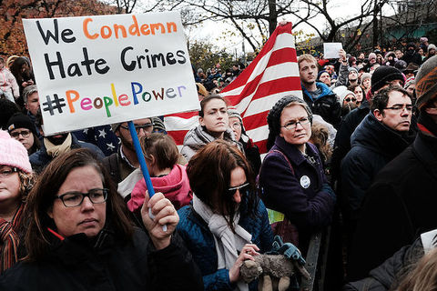 Woman surrounded by others at a rally holds a sign that reads, "We Condemn Hate Crimes"