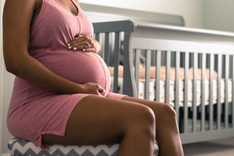 Black mother. Pregnant Black woman wearing pink dress holding her belly in a room with a white crib.