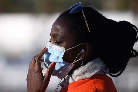 Mask. Black woman with dark hair wearing a white face mask, white scarf and orange coat.