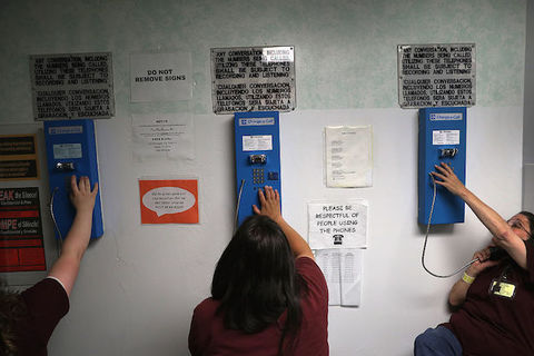 women with their backs to the camera can be seen dialing numbers on blue pay phones from prison.