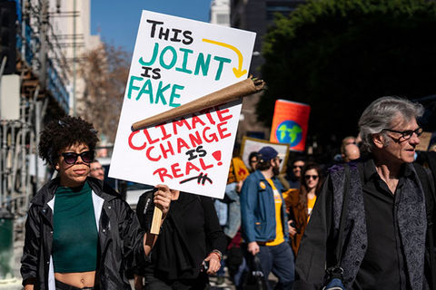 Earth Day. Black woman marching in strike holding a sign with a giant spliff that reads: "This joint is fake, climate change is real."