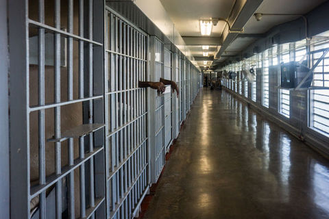 A row of prison cells with a person's arms shown hanging through some of the bars.