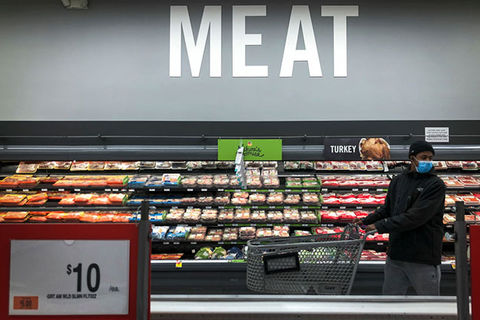 Meat. Black man wearing blue face mask, dark jacket and blue jeans, in a supermarket in front a sign that reads, "Meat."