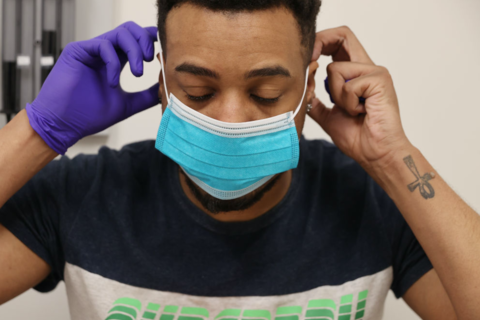 Black Man Takes Coronavirus Test. Young black man with blue mask on and one purple medical glove on in medical setting.