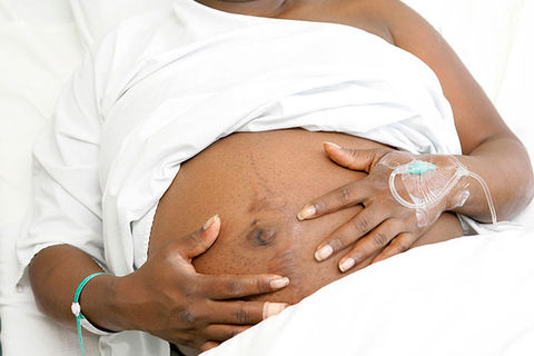 Black pregnancy. Black woman lying in white sheets holding an exposed pregnant belly.