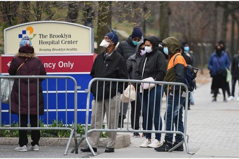 Mostly African Americans stand in line behind a metal barricade with masks on outside of The Brooklyn Medical Center