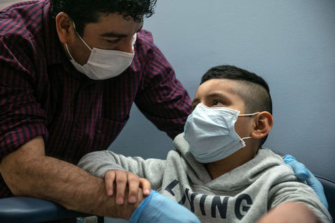 A father and son, both wearing face masks, look into each other's eyes.. 