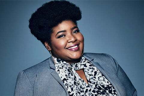 Dulcé Sloan. Black woman with dark afro wearing blue suit jacket and floral blouse.