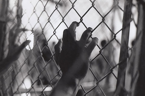 Criminal justice. Black and photo of male hands holding onto a gate.