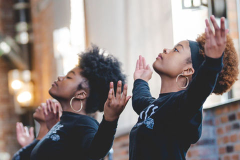 Love is Healing Fund. Two young Black women with Afros wearing black tops with both arms raised.