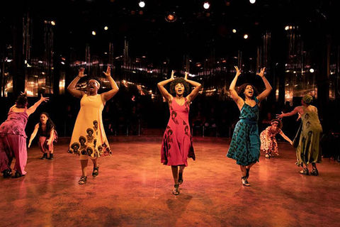 "for colored girls." Seven women of color on stage dressed in blue, orange, brown, red, yellow, green and purple. 