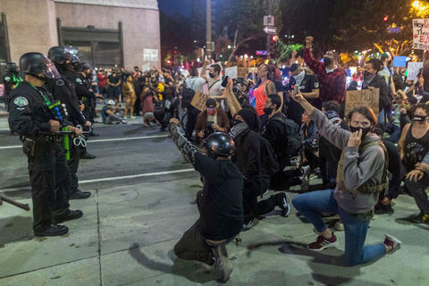 Protesters kneel before a group of armed police officers. 