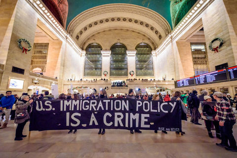 Protestors inside a large train station hold a giant sign that reads, U.S. Immigration Policy is a Crime