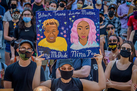 Black Trans Lives Matter rally. Man in a crowd holds up colorful drawing of Tony McDade and Nina Pop.