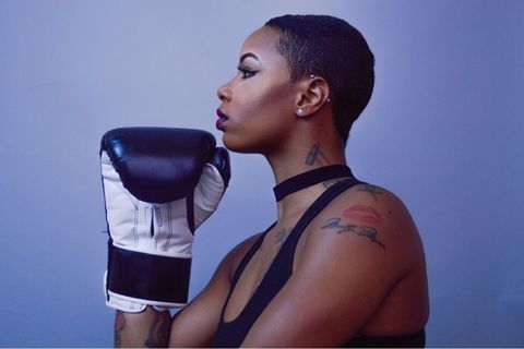 Black woman with tattoos holding her chin like the thinker with a boxing glove