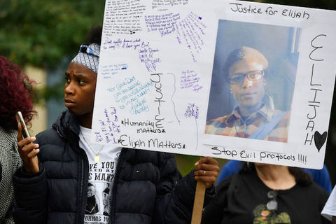Black protester holds poster showing image of young Black man wearing black eyeglasses. 