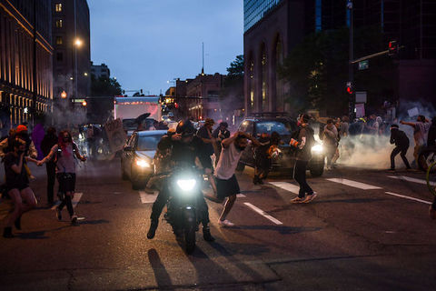 Demonstrators run through a city street as police officers deploy tear gas behind them. 
