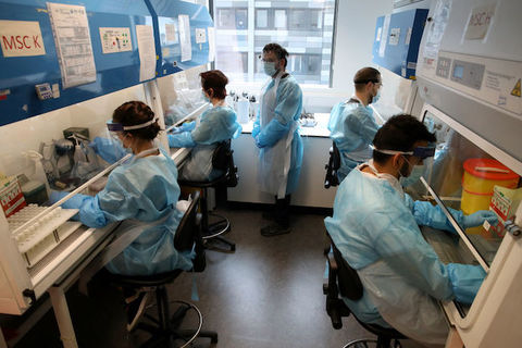 Researchers wearing blue protective gear sit and work in scientific lab.