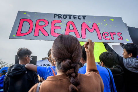 A woman with a long braid holds a sign that reads, "Protect Dreamers"