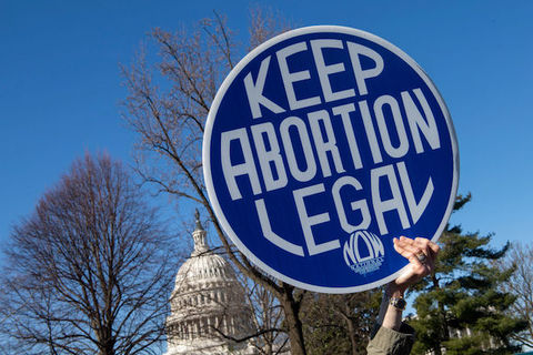 A hand holds a sign that reads "Keep Abortion Legal" in front of the US Capitol and under a clear blue sky