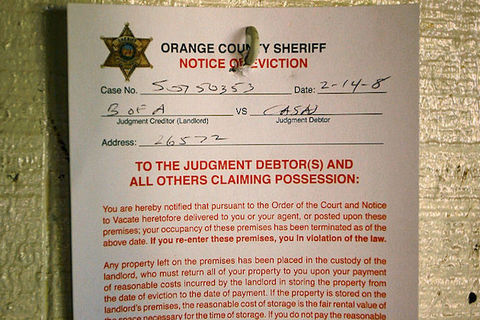A paper eviction notice from the Orange Country Sheriff hanging on a door.