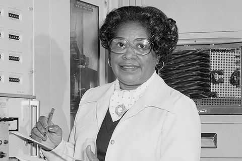 Mary Jackson. Black and white photo of Black woman with dark hair wearing white lab coat and glasses, holding a notepad and pen.