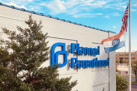Planned Parenthood. Exterior of building with blue letters and logo reading Planned Parenthood next to a flying American flag.