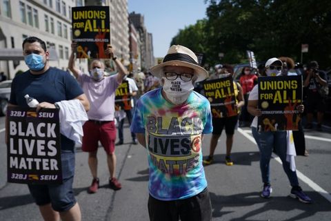 Close up of demonstrator at Strike for Black Lives rally in rainbow tie-dye shirt and with a "Black Lives Matter" banner on his shirt.
