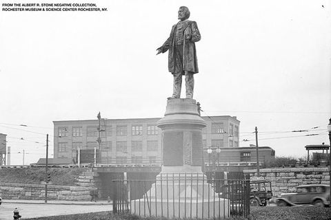 Frederick Douglass monument. Black and white photo of statue of a Black man on a tall pedestal in the city of Rochester, N.Y.