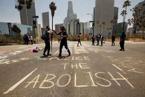 Abolish the police is written in chalk on a Los Angeles street as protestors stand nearby and shake hands. 