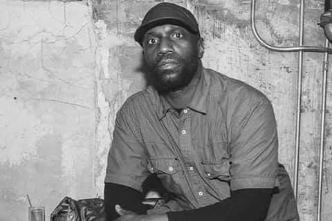 Malik Basit. Black and white photo of Black man wearing a hat and dark shirt.