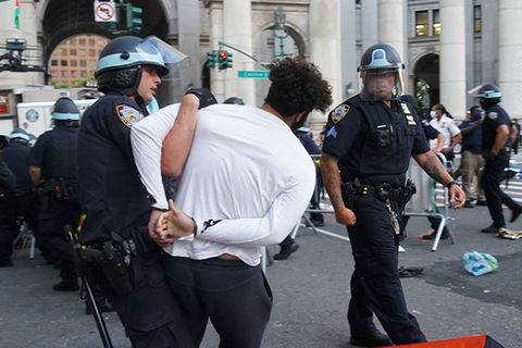 Police Force. Police officer in uniform arresting a Black man with curly hair, white shirt and black pants at a protest.