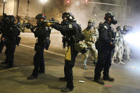 federal officers point large black weapons at protesters 