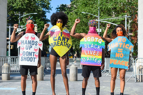 Protest ARt. Four models of color stand side-by-side wearing colorful body placards with BLM slogans.