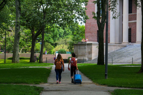 two people with luggage walk through a college campus. 