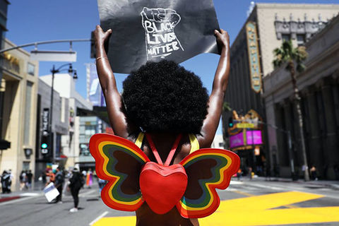 Strike for Black Lives. Black woman with big dark Afro holding a 'Black Lives Matter' sign and waring a heart shaped, butterfly shaped backpack.